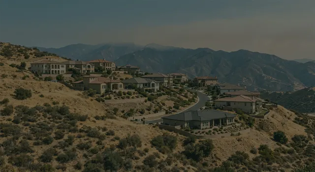 A California hillside neighborhood near dry hills with smoke in the distance